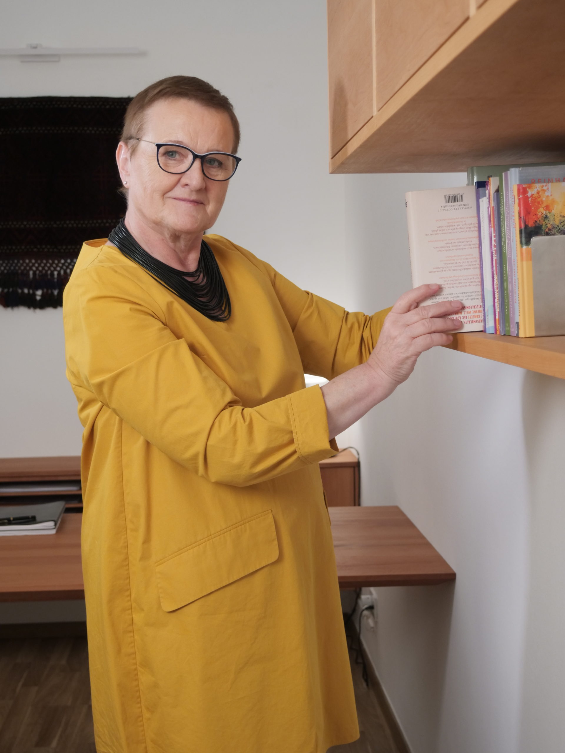 Psychotherapeutin-Elfriede-Ulbl-Bücherregal Psychotherapeutin Elfriede Ulbl nimmt ein Buch aus einem Bücherregal